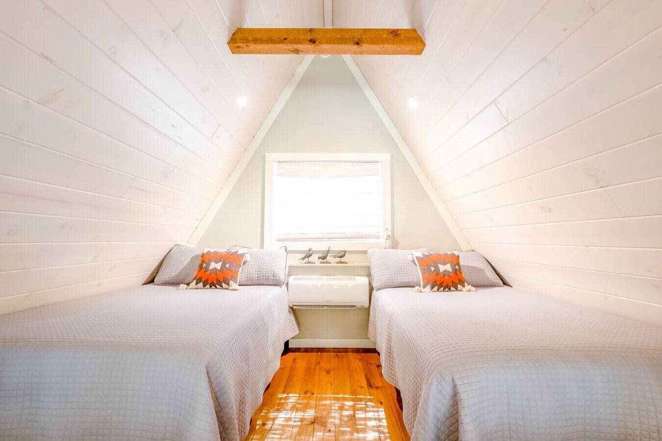 Un dormitorio acogedor en el ático, con dos camas, una ventana y techo con vigas de madera.