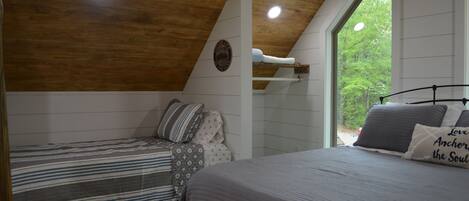 A bedroom with two beds, a wooden ceiling, a window with a view of trees, and a shelf with a white object.