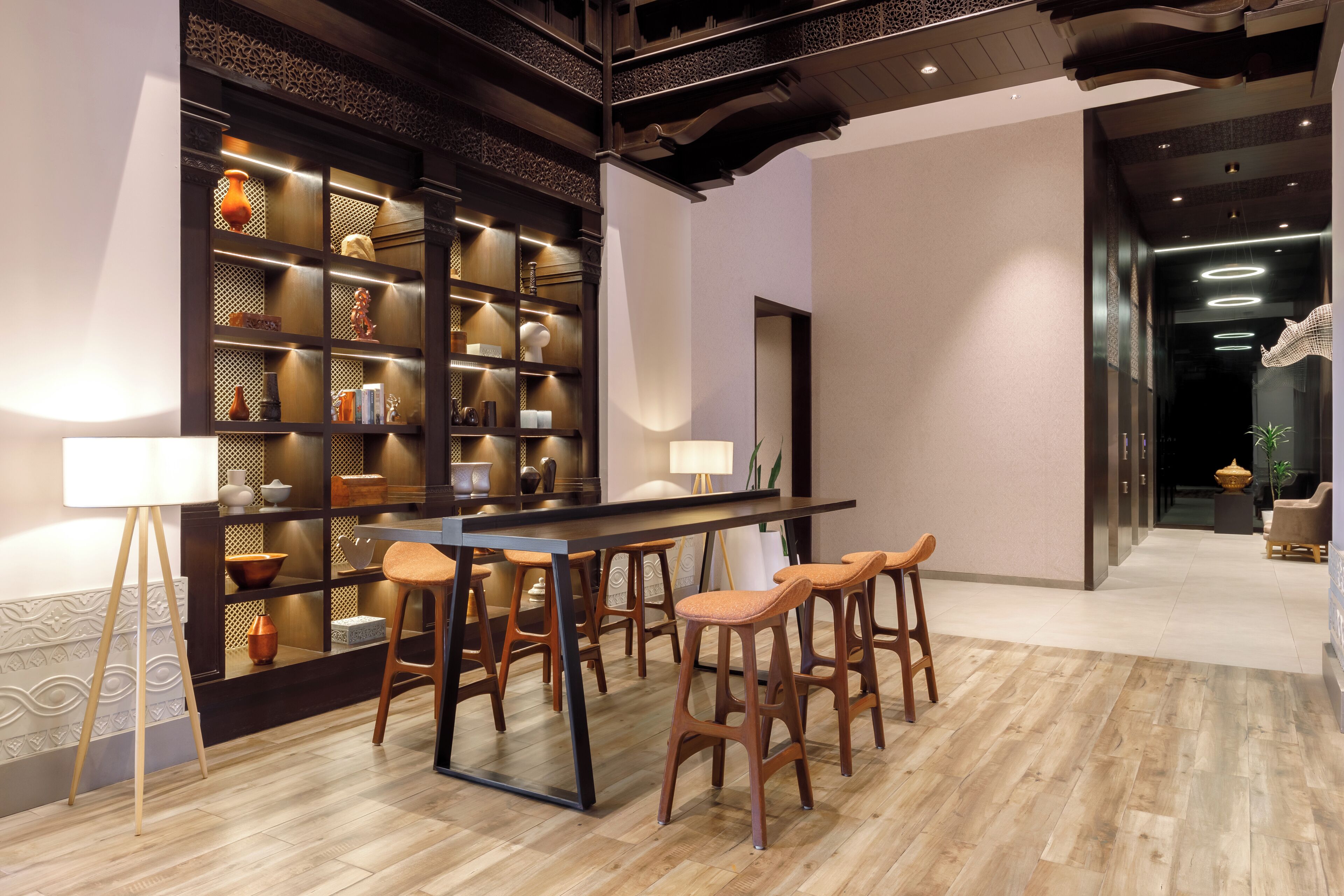 A modern interior with a wooden bar area, stools, a large bookshelf, and a patterned floor.