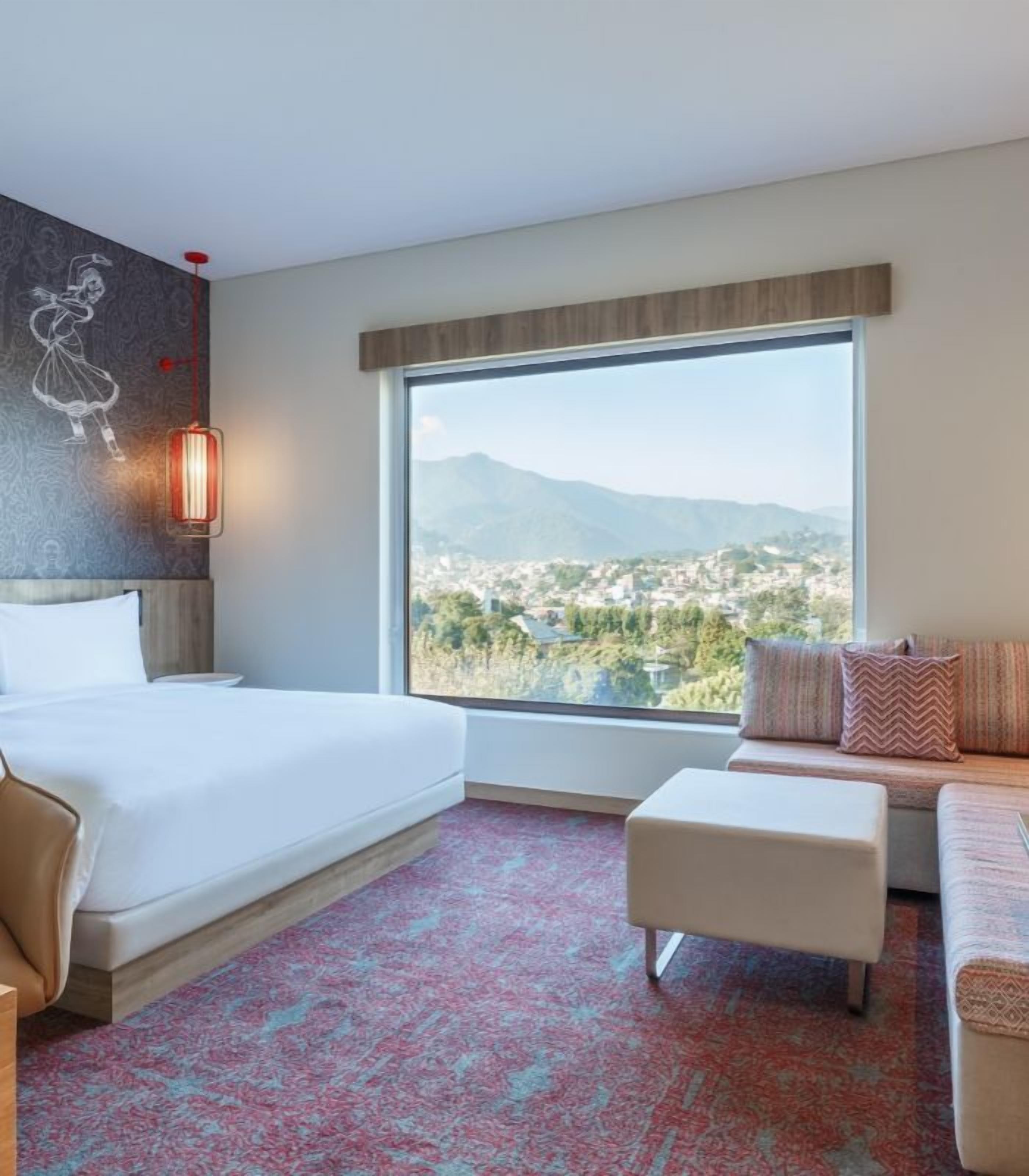 A hotel room with a large window, a bed, a sofa, and a small table.