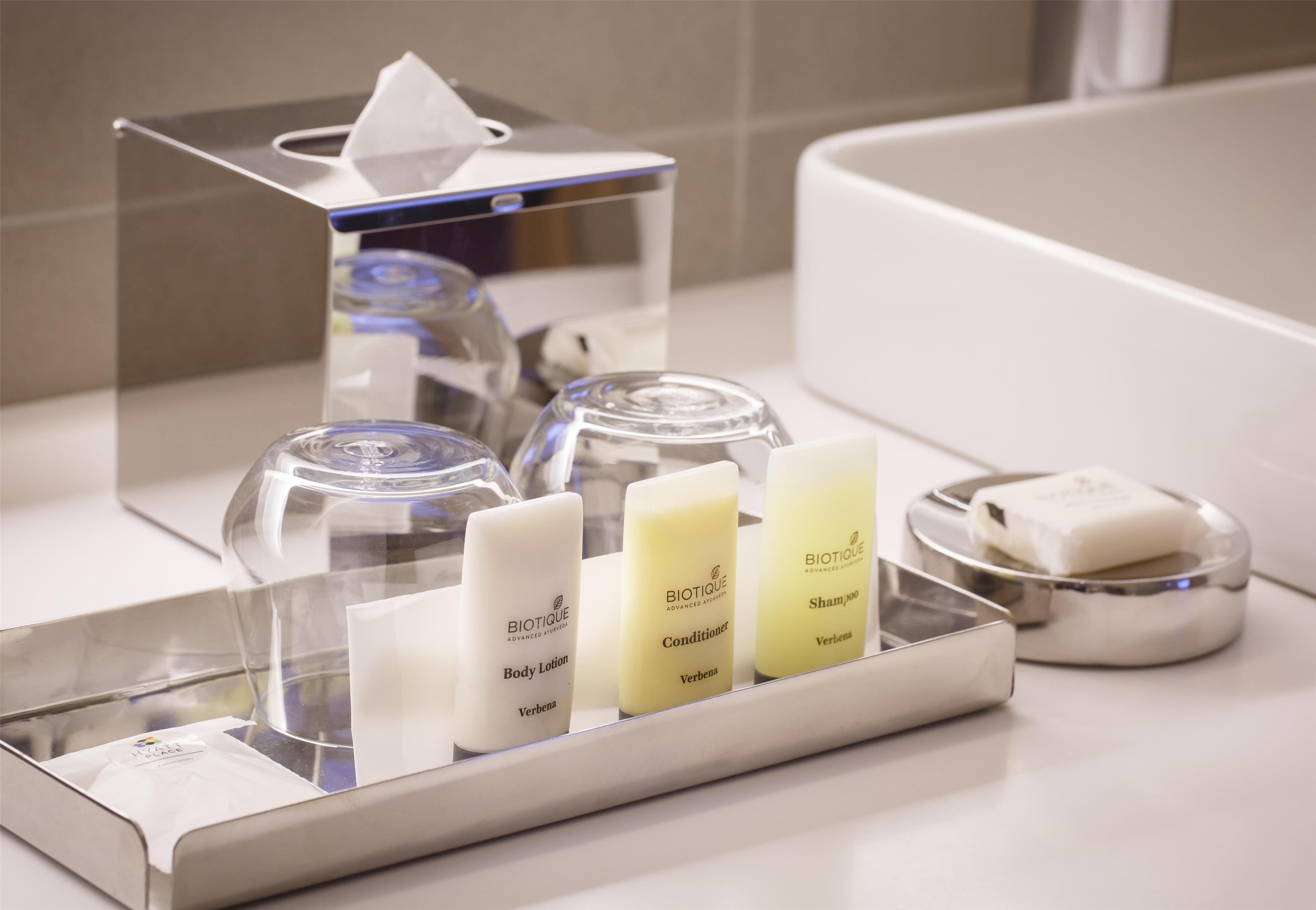 A bathroom vanity with a mirror, a tissue dispenser, and three bottles of Biotique products: body lotion, conditioner, and shampoo.