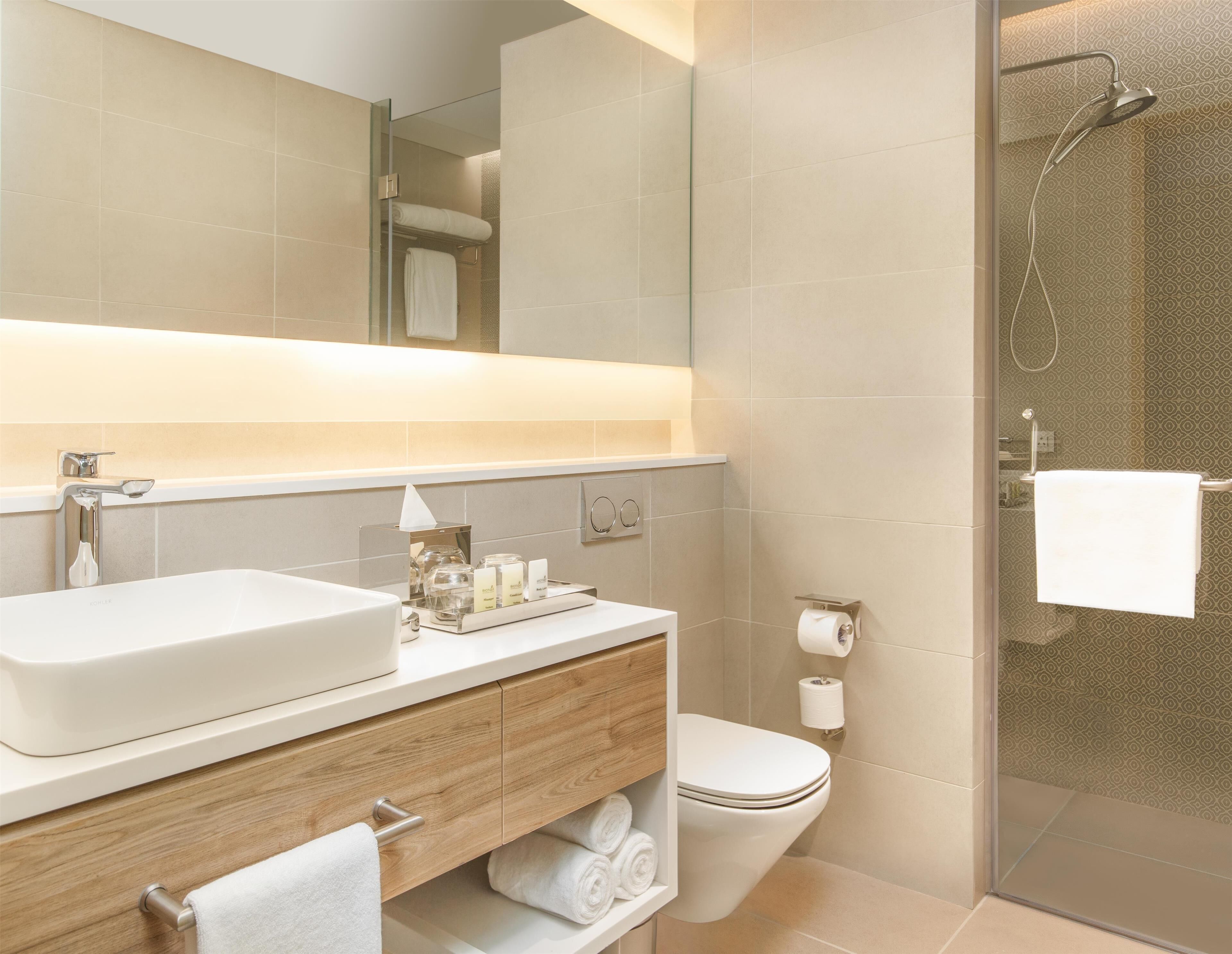 A modern bathroom with a large mirror, a sink, a toilet, and a shower.