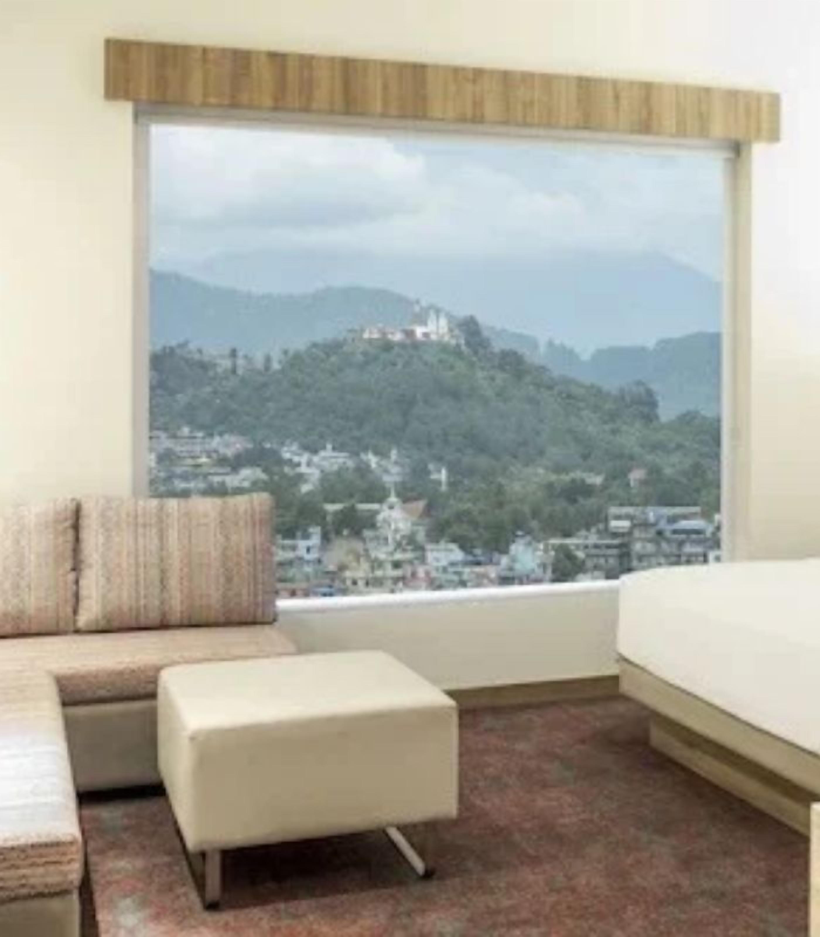 Una habitación de hotel con un ventanal grande, un sofá, un reposapiés y una cama.