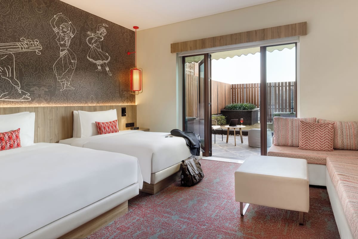 A hotel room with two beds, a sofa, a small table, and a balcony with a view of the outdoors.