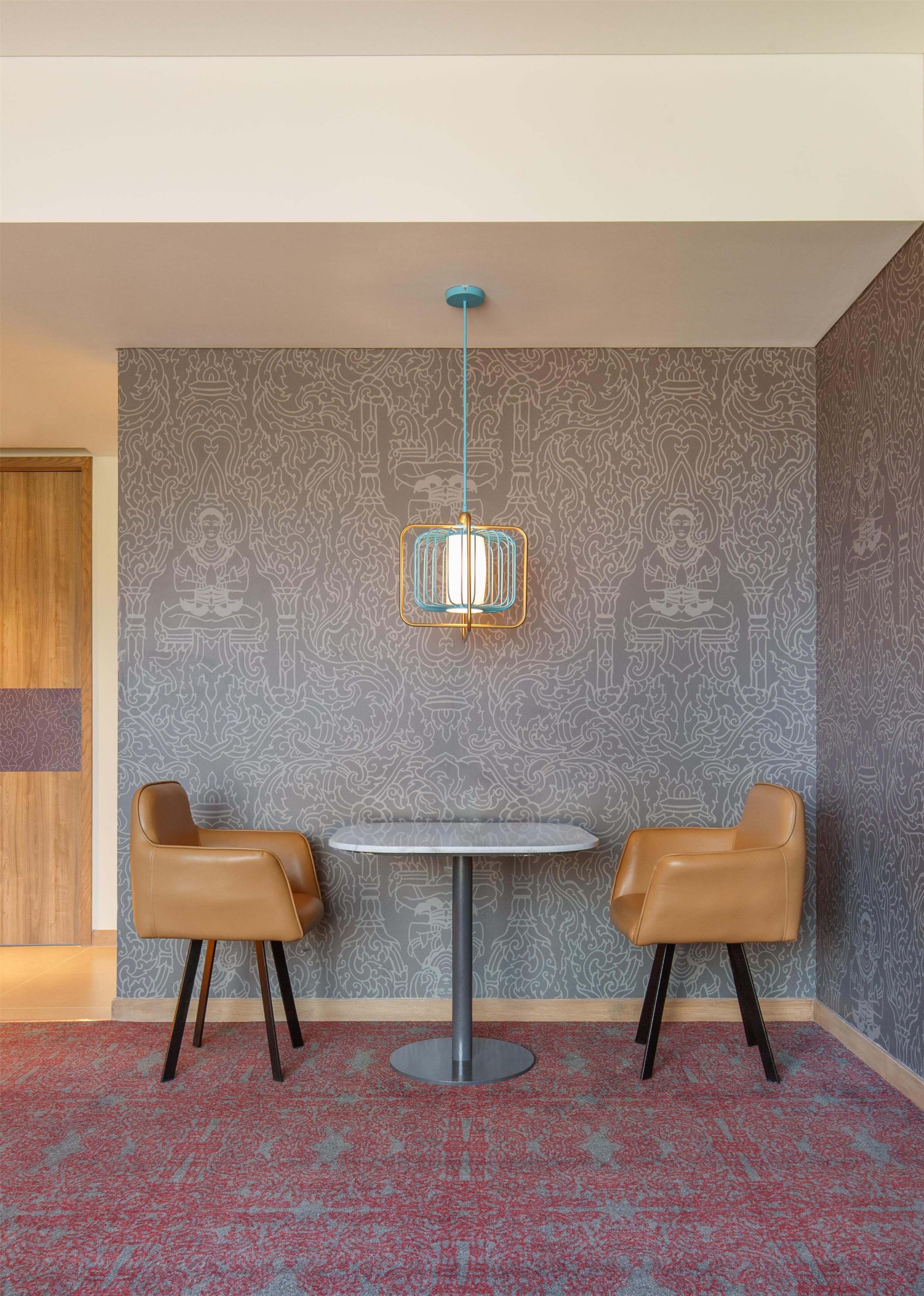 A room with a round table, two leather chairs, a patterned wall, and a hanging light fixture.