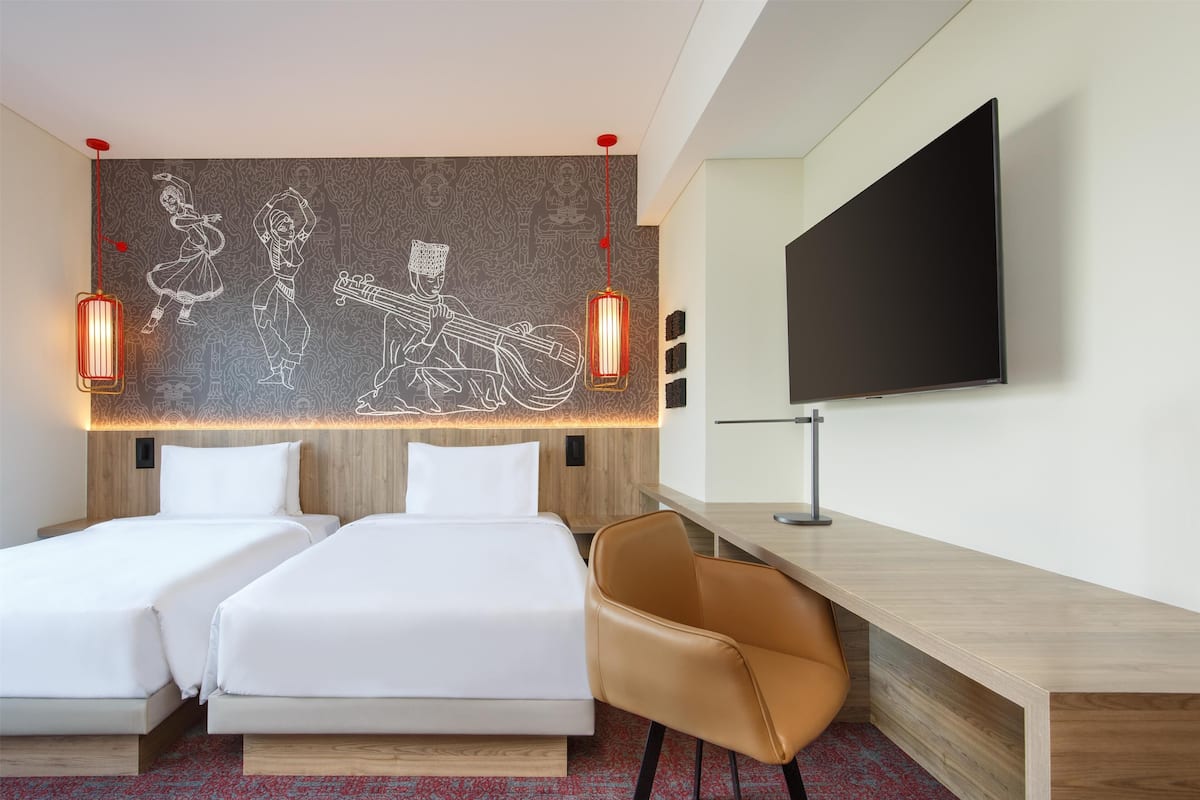 A hotel room with two beds, a desk, a chair, a TV, and a wall mural.