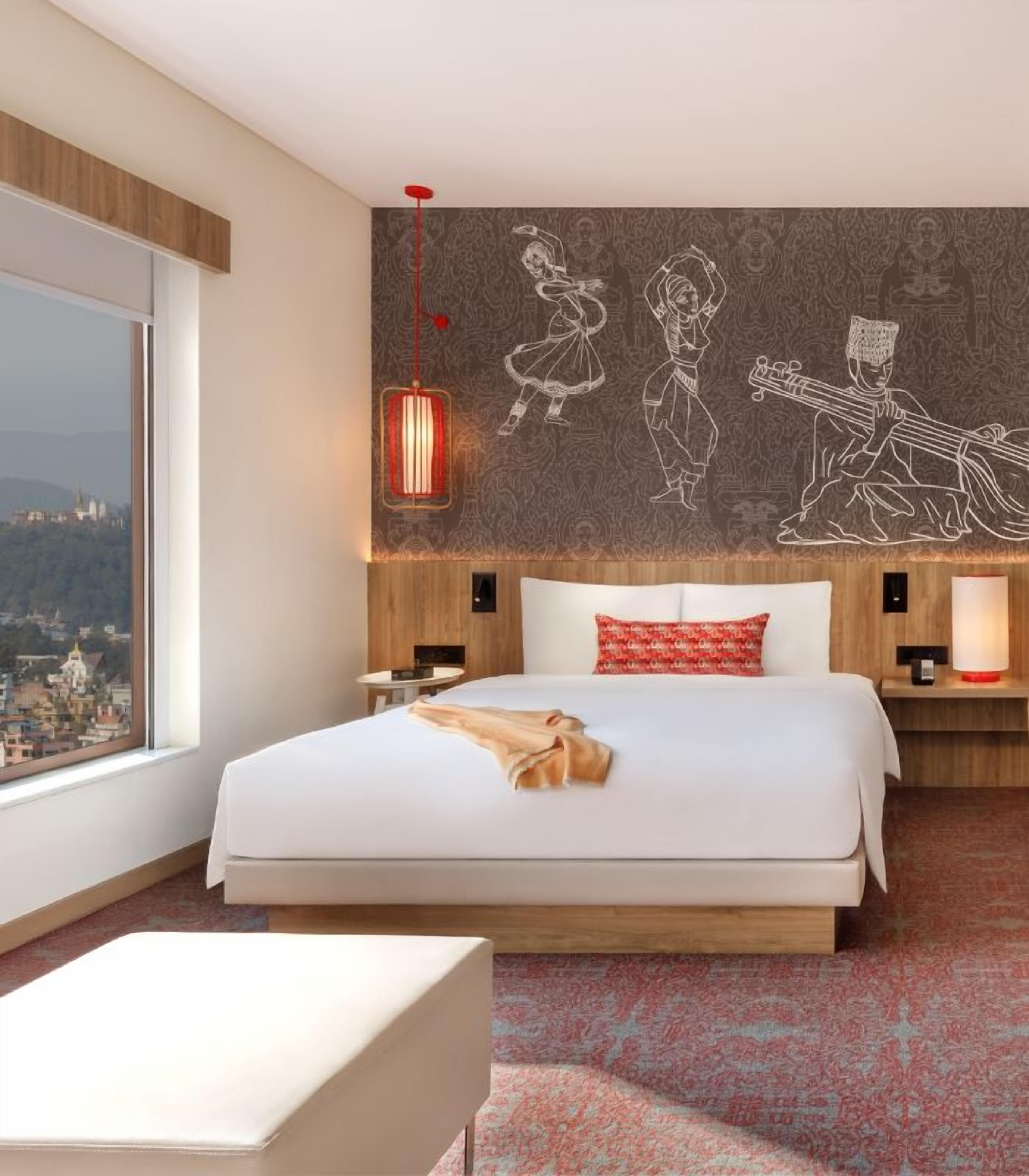 A hotel room with a large bed, a view of a cityscape, a patterned wall, and a red pendant light.