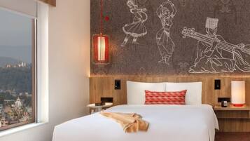 A hotel room with a large bed, a view of a cityscape, a patterned wall, and a red pendant light.