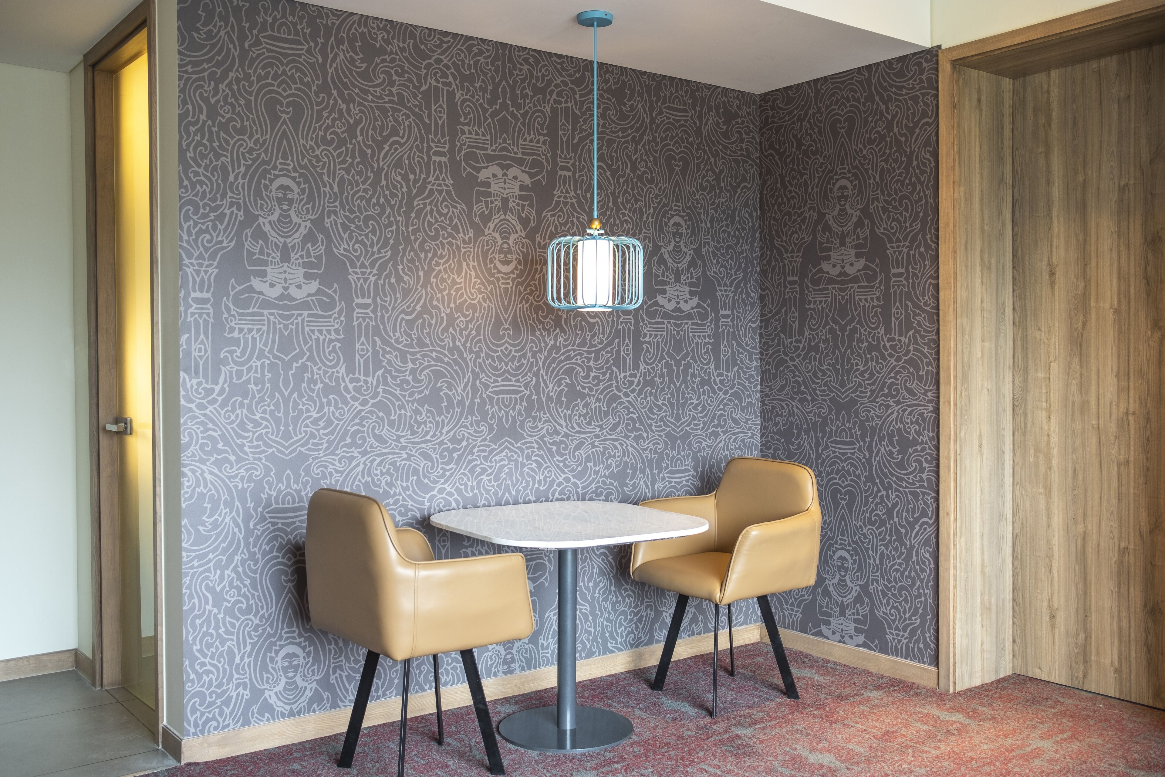 A room with a patterned wallpaper, a round table with two chairs, a hanging light fixture, and a wooden door.