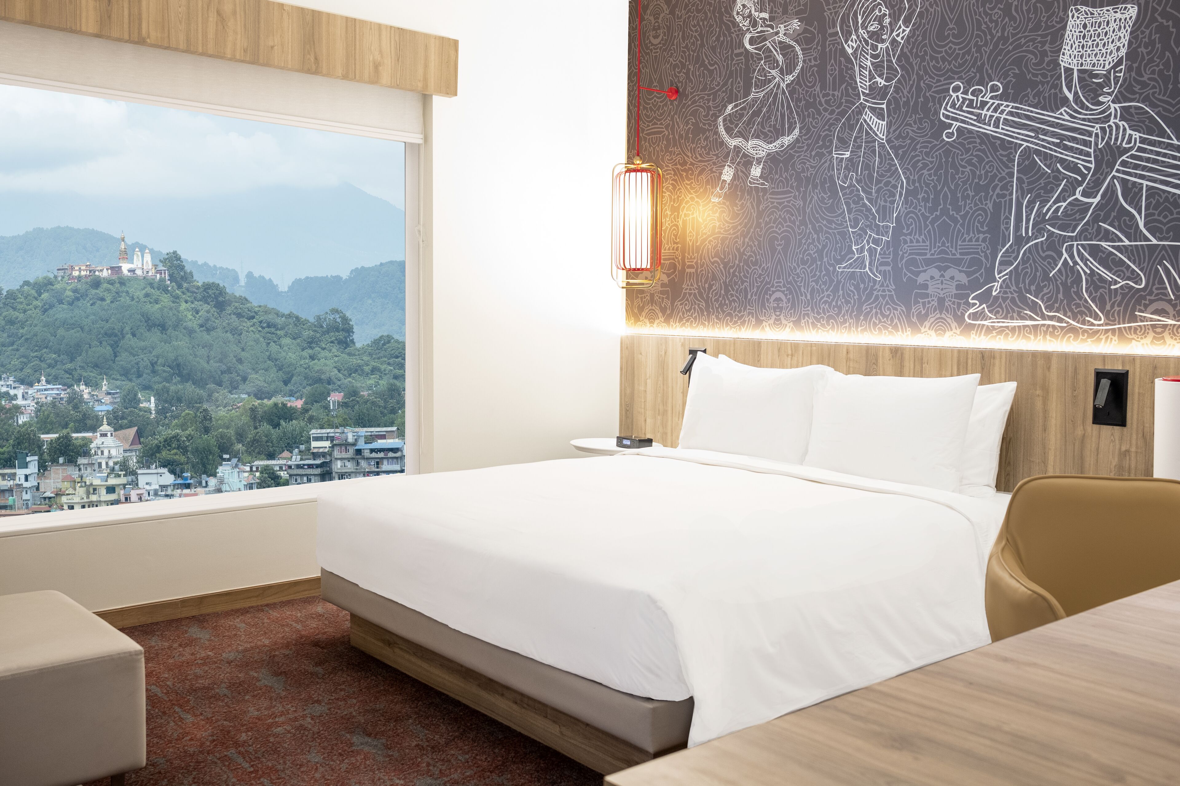 A hotel room with a large bed, a wooden headboard, a view of a cityscape, and a wall mural.