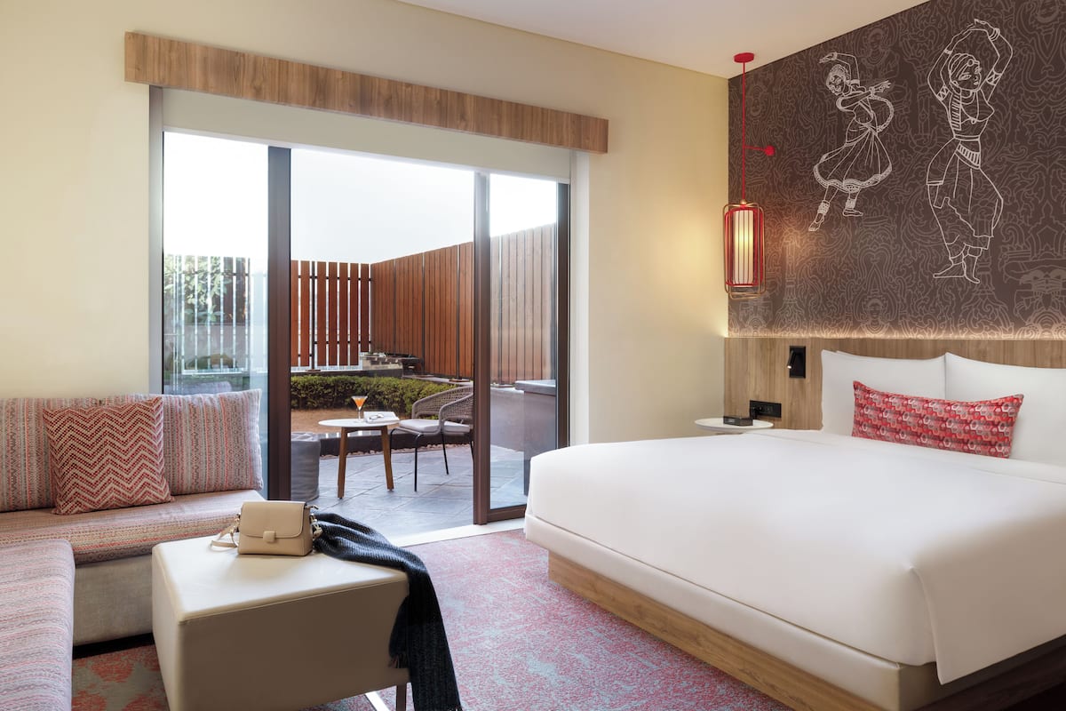 A modern hotel room with a large bed, a sofa, a small table, and a view of the outdoor patio.