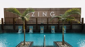 Una piscina con cerco de madera y palmeras, y la palabra "ZING" en el cerco.