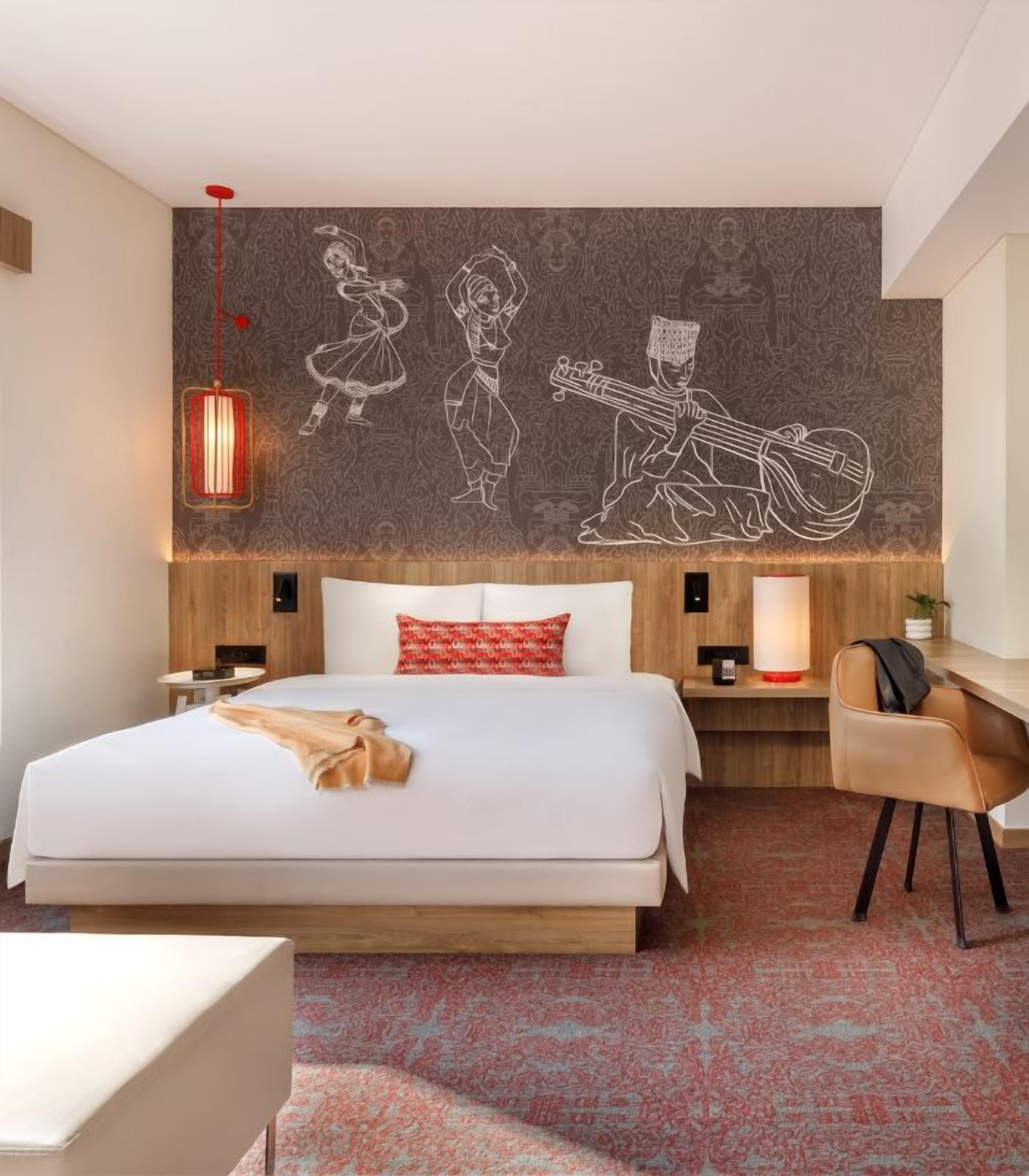 Una habitación de hotel con una cama grande, un escritorio, una silla, un tapete rojo estampado y una pared con un mural.