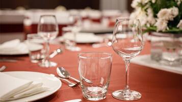 Une table à manger dressée avec de l’argenterie, des assiettes blanches et des verres transparents, et un vase rempli de fleurs blanches en arrière-plan.