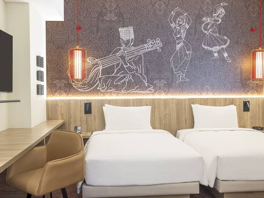 Hotellihuone, jossa on kaksi sänkyä, työpöytä ja seinä, joka on koristeltu koristeellisella seinämaalauksella.