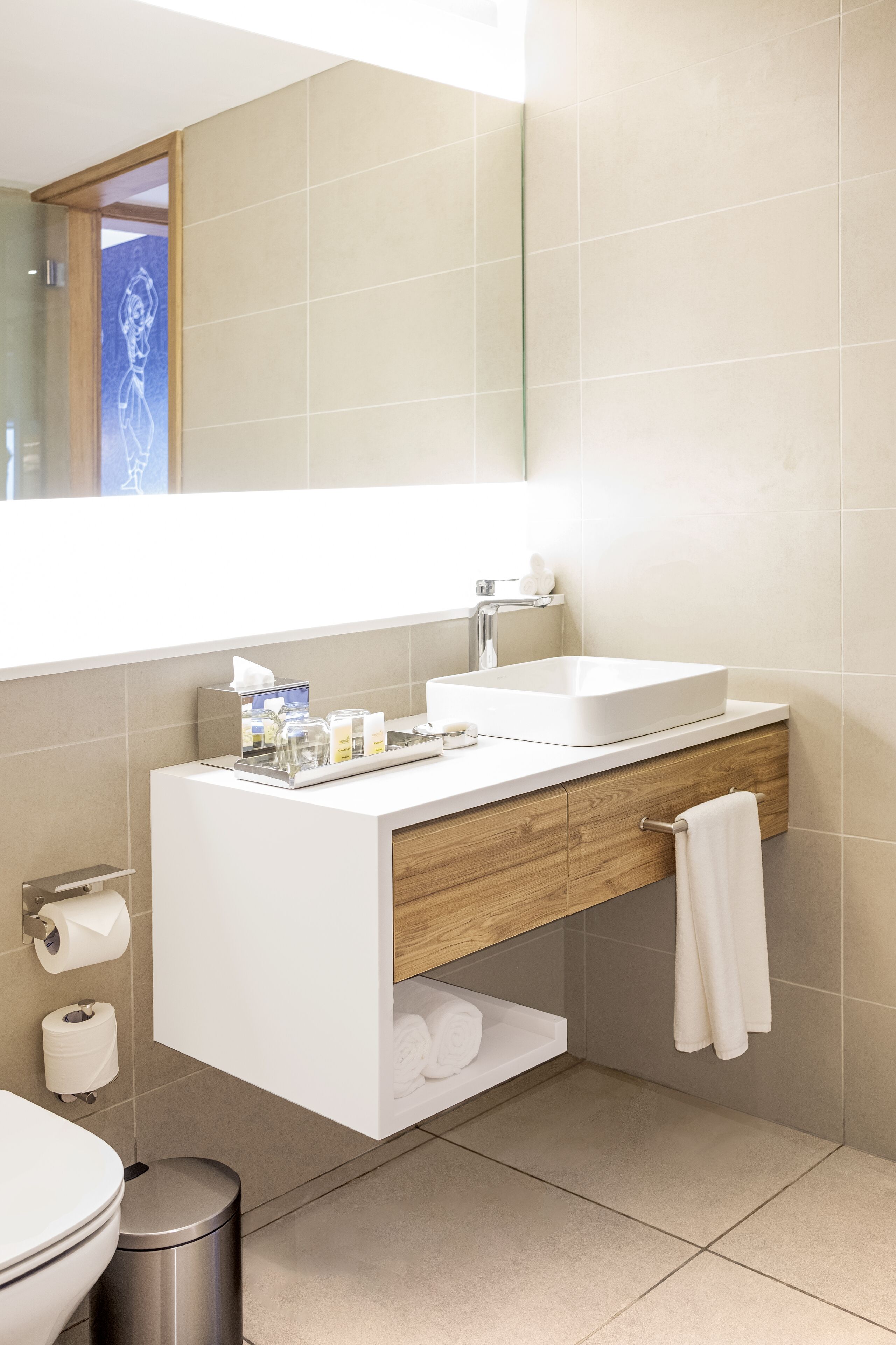 Un baño moderno con lavabo blanco, tocador de madera y un espejo grande.
