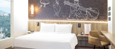 A modern hotel room with a large bed, a desk, and a chair. There is a wall mural depicting dancers and a musician.