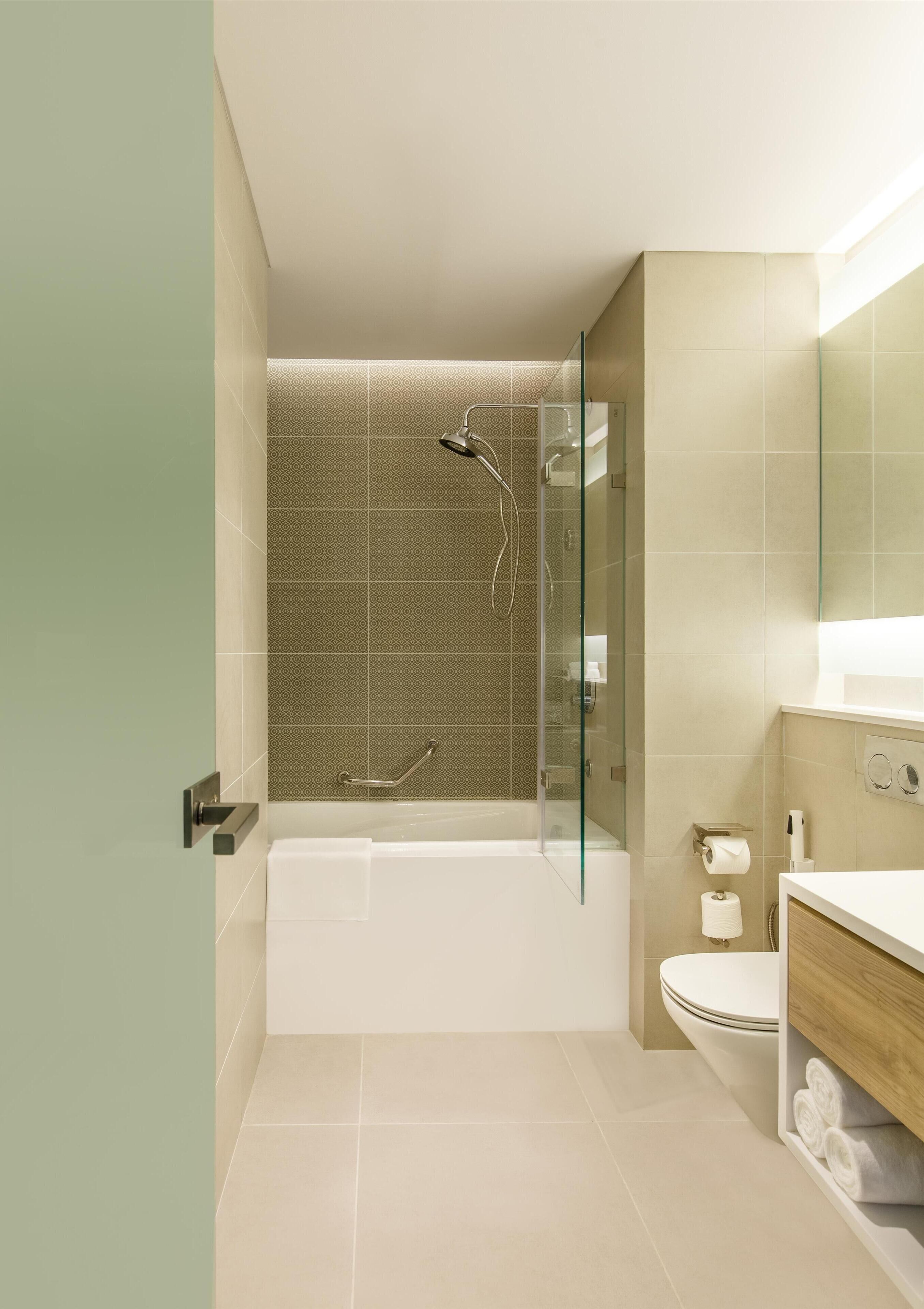 A modern bathroom with a glass-enclosed shower, a white bathtub, and a wooden vanity with a mirror.