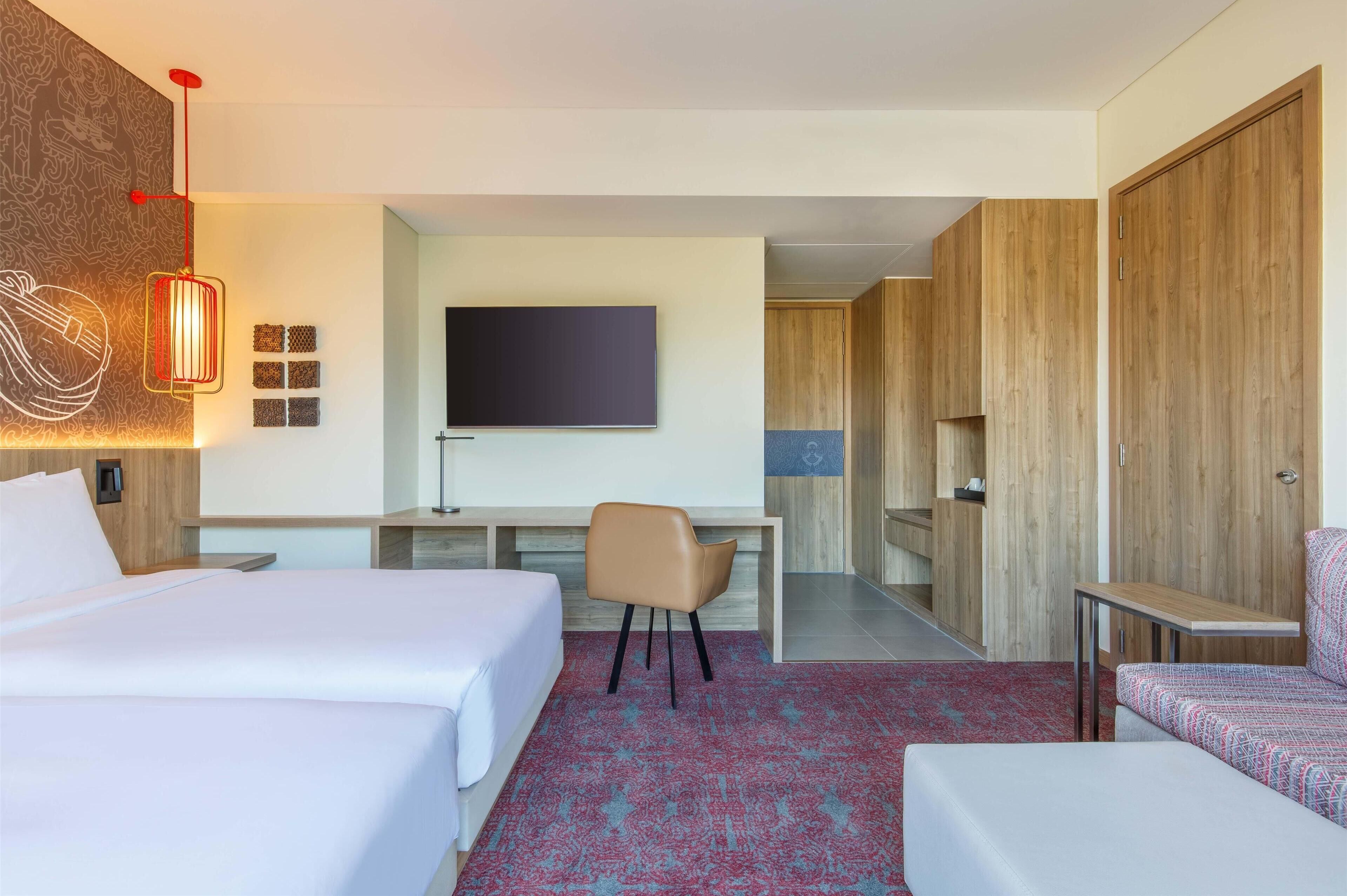 A hotel room with a bed, a desk, a chair, a TV, and wooden wardrobes.