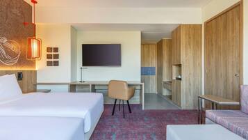 Habitación de hotel con cama, escritorio, silla, televisor y armarios de madera.