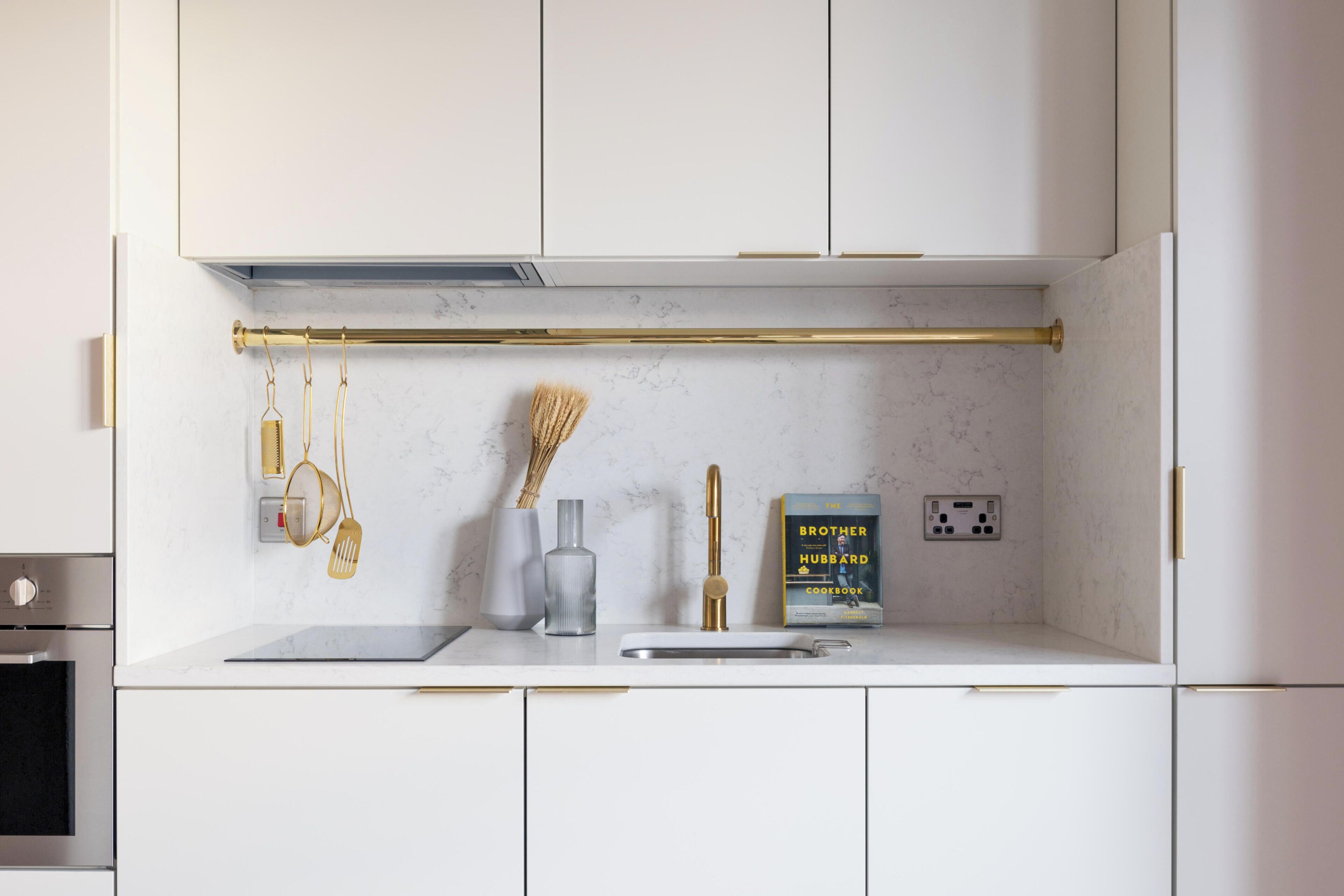 A modern kitchen with white cabinets, a marble backsplash, a gold faucet, and a cookbook on the counter.