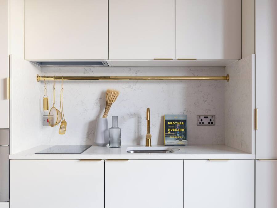 A modern kitchen with white cabinets, a marble backsplash, a gold faucet, and a cookbook on the counter.