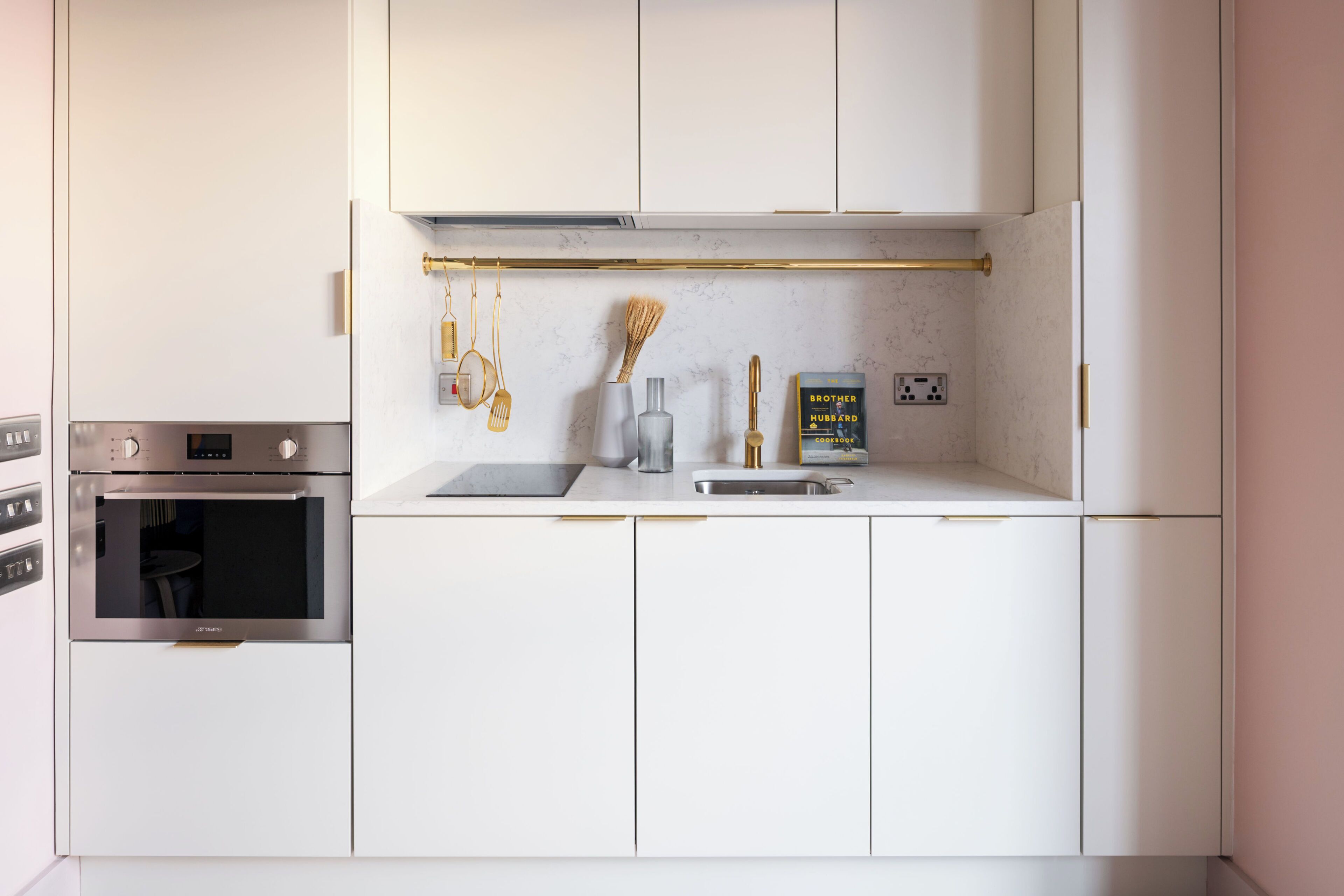 Une cuisine moderne avec des armoires blanches, un four encastré, une hotte de cuisinière en acier inoxydable et un plan de travail aux lignes épurées.