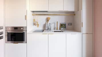 Une cuisine moderne avec des armoires blanches, un four encastré, une hotte de cuisinière en acier inoxydable et un plan de travail aux lignes épurées.