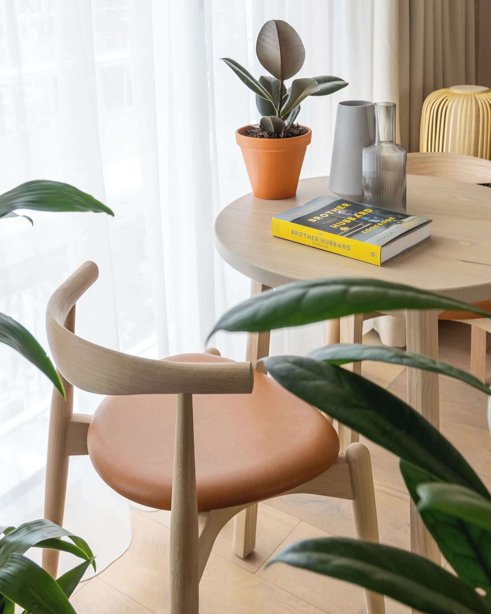 A wooden dining table with a potted plant, a book, and a lamp.