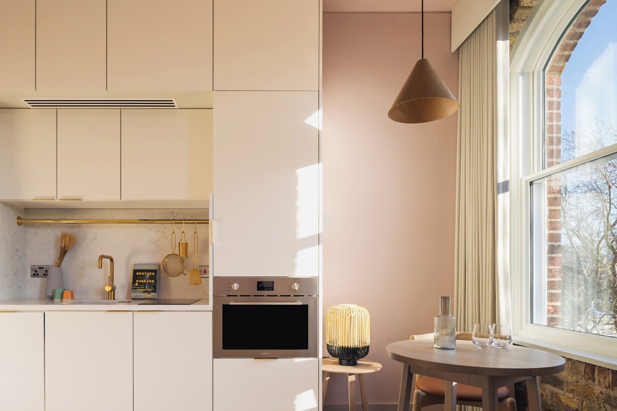 A modern kitchen with a built-in oven, a hanging light fixture, and a view of a brick building through a large window.