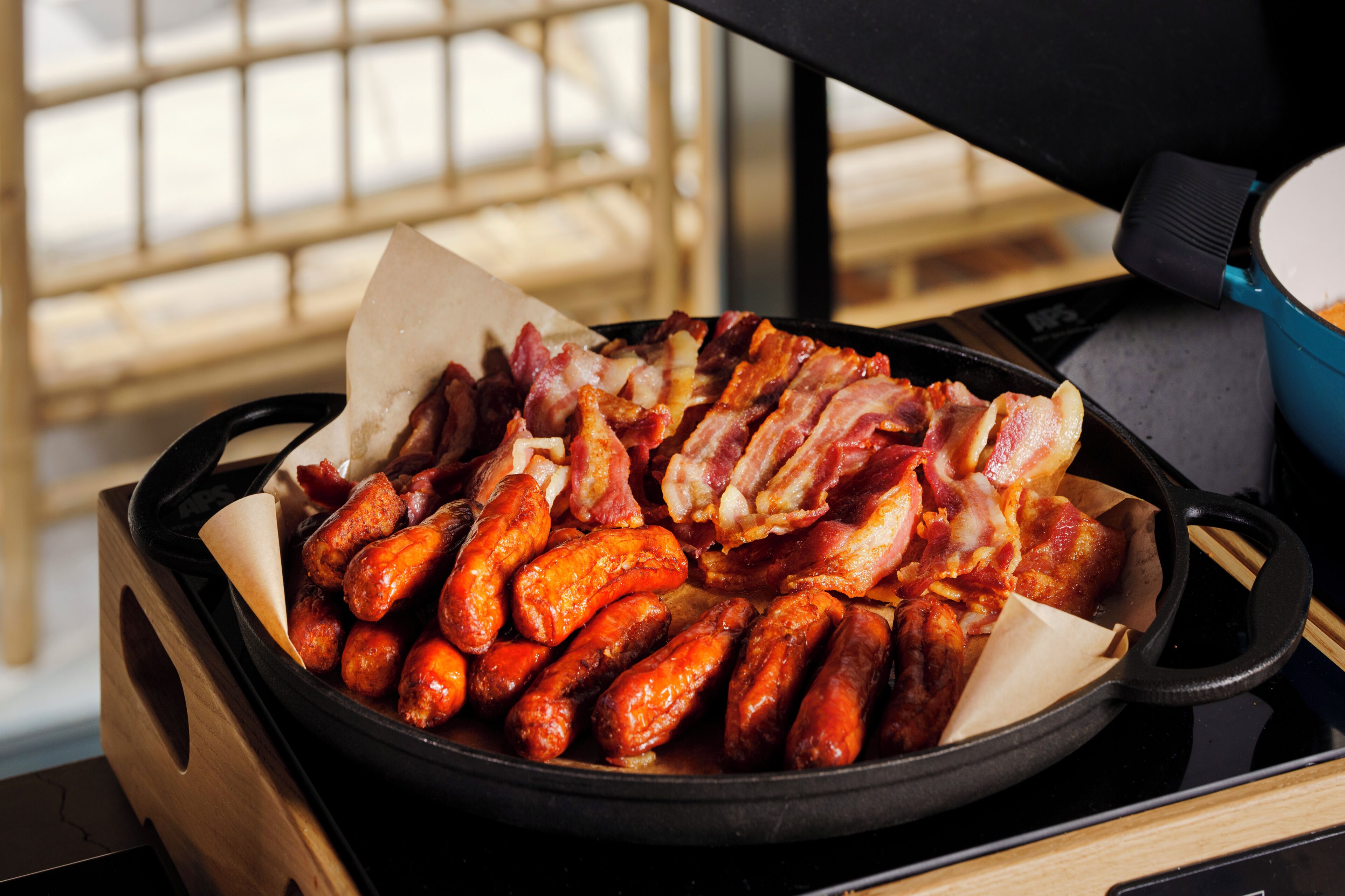 A cast iron skillet filled with cooked sausages and bacon on a stove.
