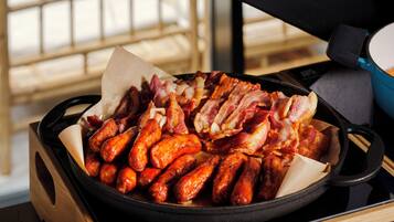 A cast iron skillet filled with cooked sausages and bacon on a stove.