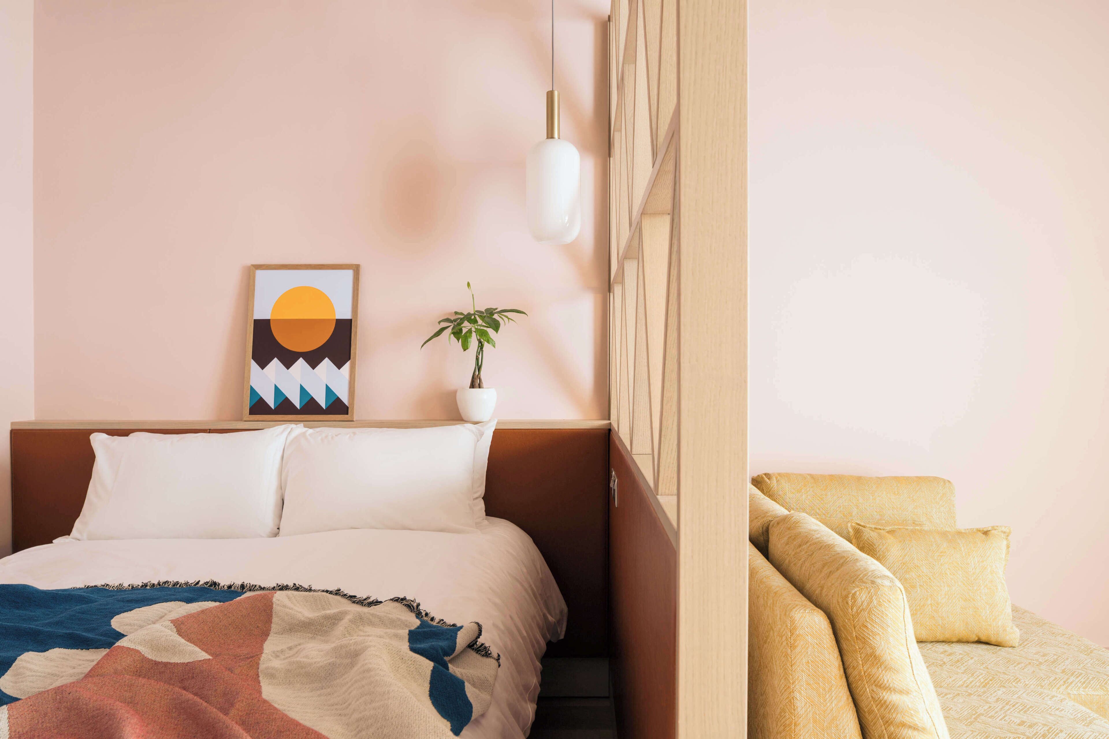 A bedroom with a bed, a bedside plant, a wall-mounted artwork, and a sofa.
