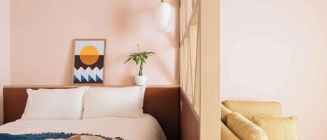 Un dormitorio con una cama, una planta en la mesita de noche, una obra de arte en la pared y un sofá.