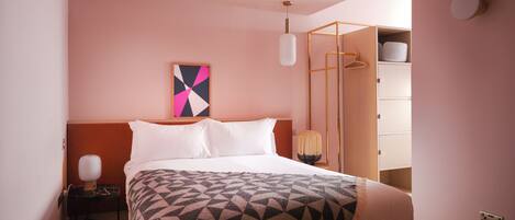 Une chambre à coucher comprenant un lit, une table de chevet, une lampe, une couverture à motifs géométriques, une œuvre d’art murale et une armoire.