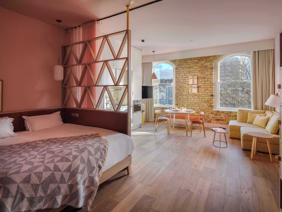 Una camera d'albergo con un letto grande, una zona pranzo, un divano e un muro in pietra.