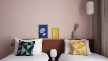 A hotel room with two beds, a nightstand, a lamp, and artwork on the wall.