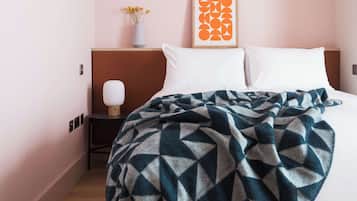 A hotel room with a bed, a nightstand, a lamp, a framed artwork, and a vase with flowers.
