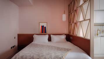 A hotel room with a large bed, a headboard, a framed artwork, a hanging light, and a view of the bathroom.