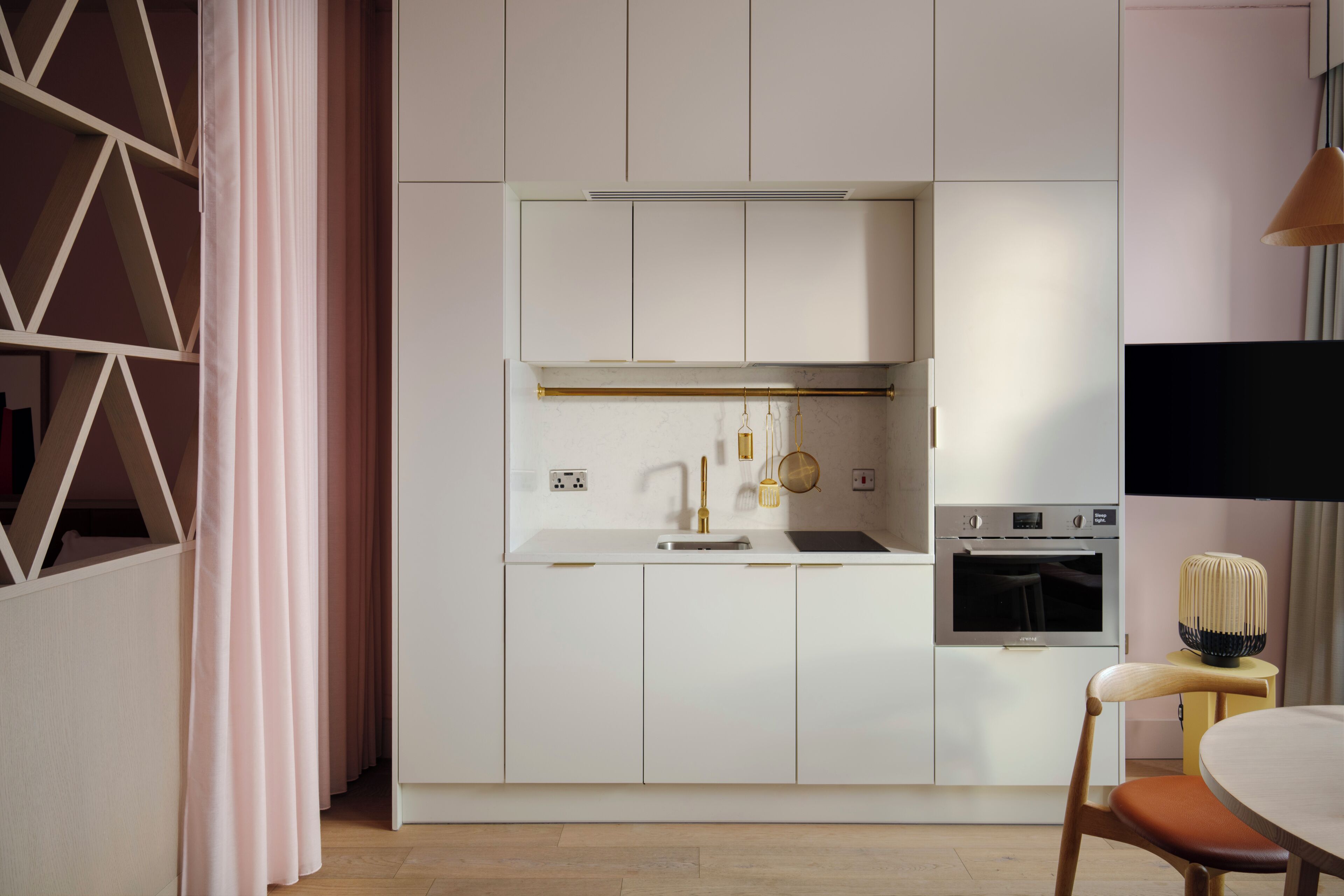 A modern kitchen with white cabinetry, a built-in oven, and a dining area with a table and chair.