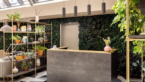 A reception desk with a grey countertop and gold accents, surrounded by shelves with various potted plants and a wall covered in greenery. - Zanzibar Locke (Dublin)