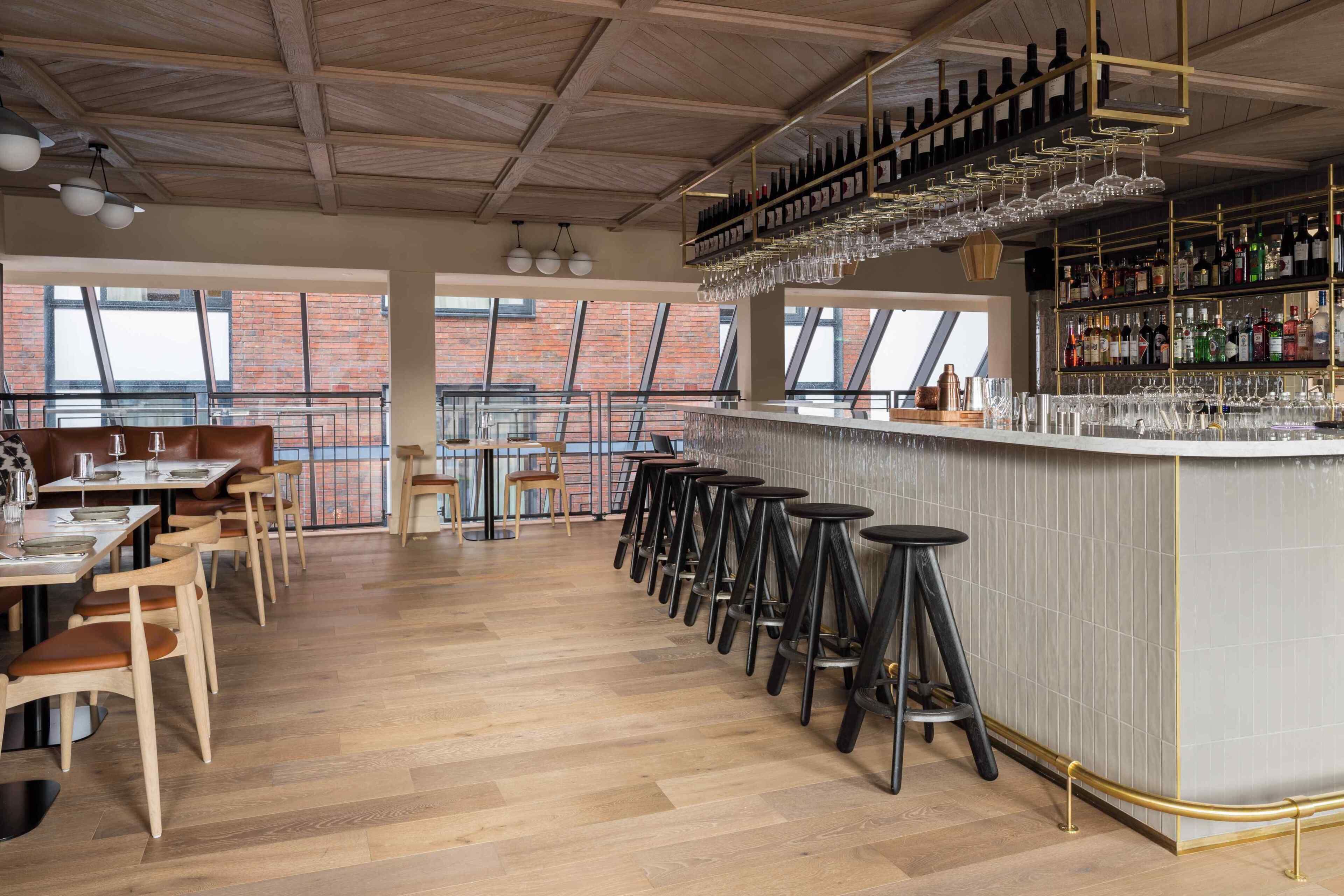 A bar area with stools, a bar counter, and shelves of bottles and glasses.
