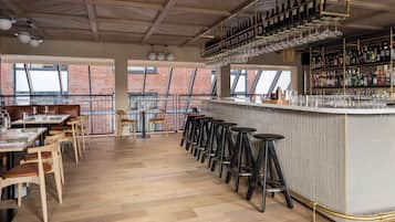 A bar area with stools, a bar counter, and shelves of bottles and glasses.