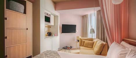 A hotel room with a bed, a sofa, a TV, a minibar, and a wardrobe.