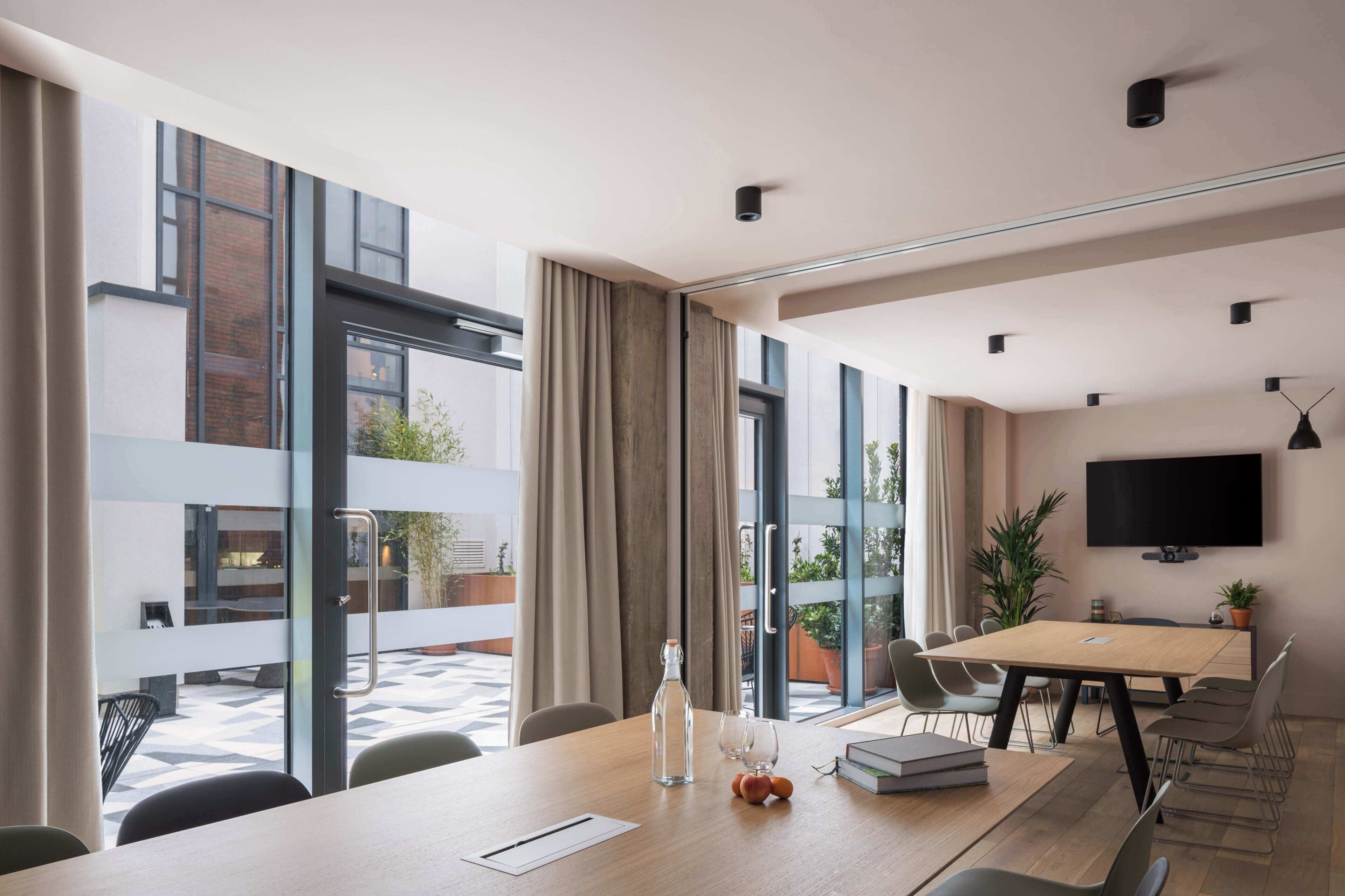A modern conference room with a large table, chairs, a television, and large windows.