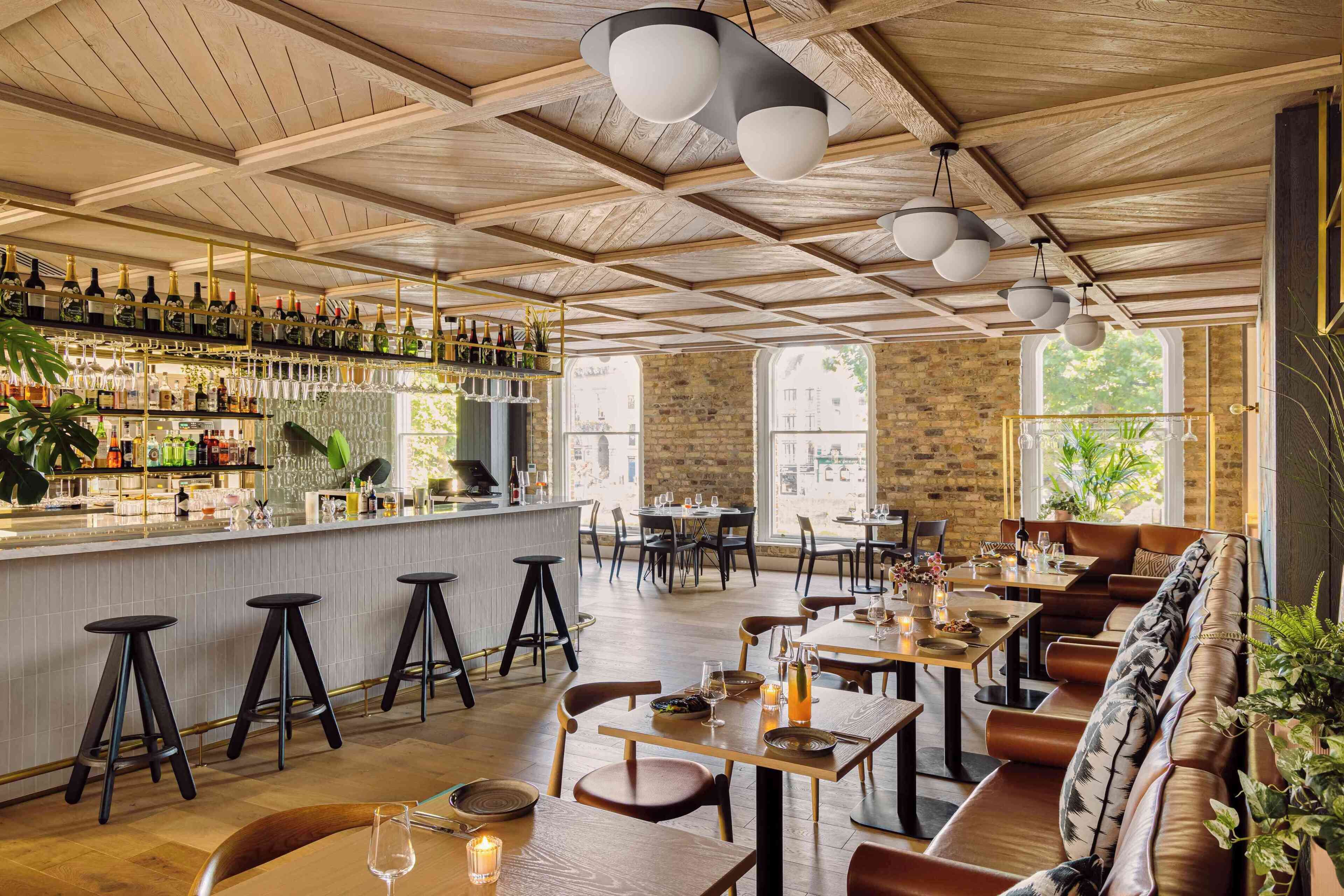 Un restaurant avec des poutres en bois au plafond, un bar où sont exposées les bouteilles, et des tables et des chaises pour les clients.