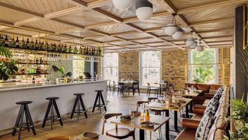 A restaurant with wooden ceiling beams, bar area with bottles, and seating with tables and chairs.
