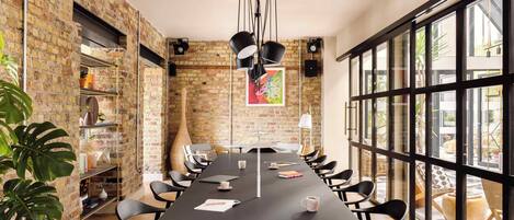 A conference room with a long table, black chairs, a brick wall, and large windows.