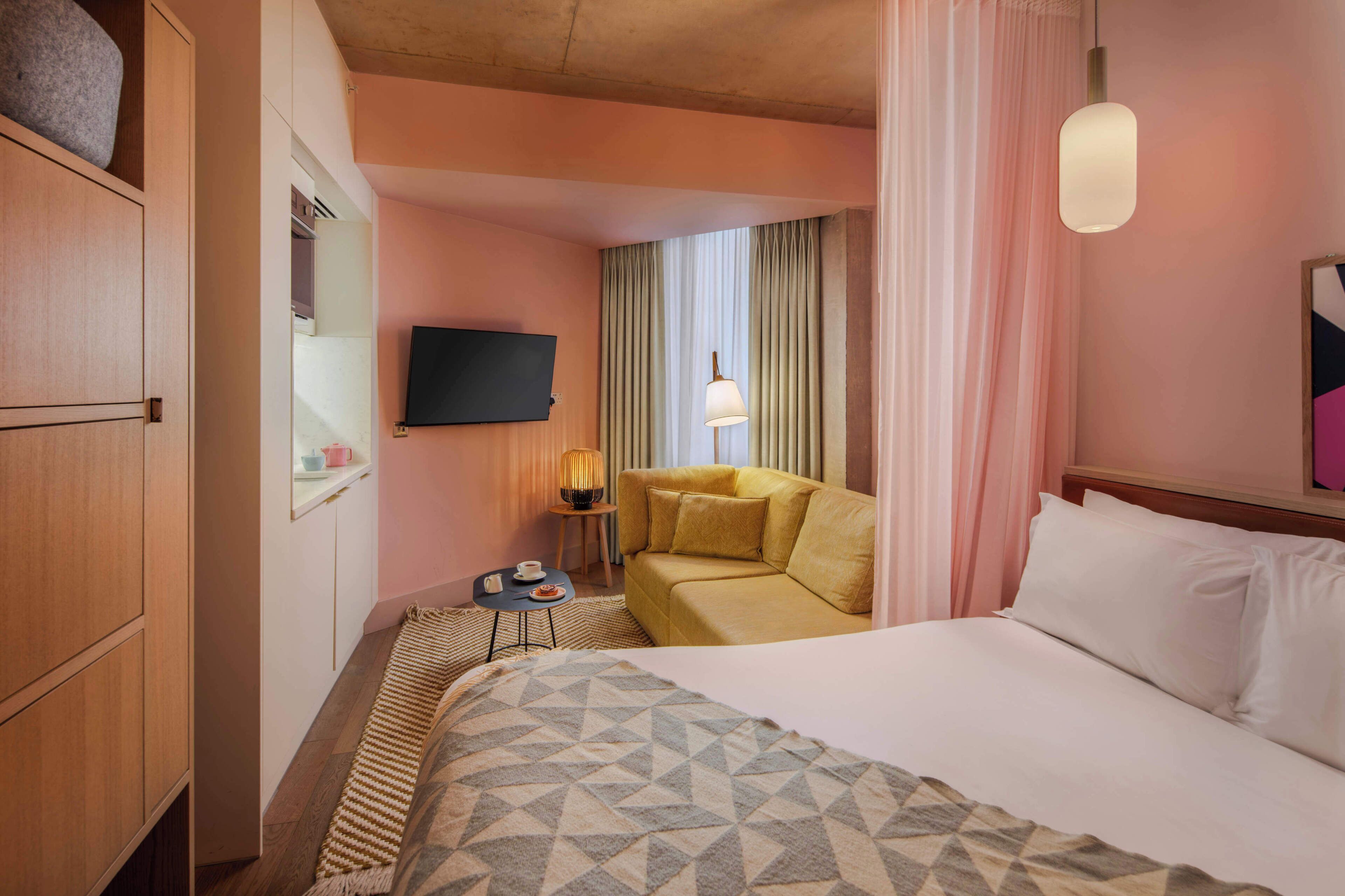 A hotel room with a bed, a sofa, a television, a lamp, and a small table.