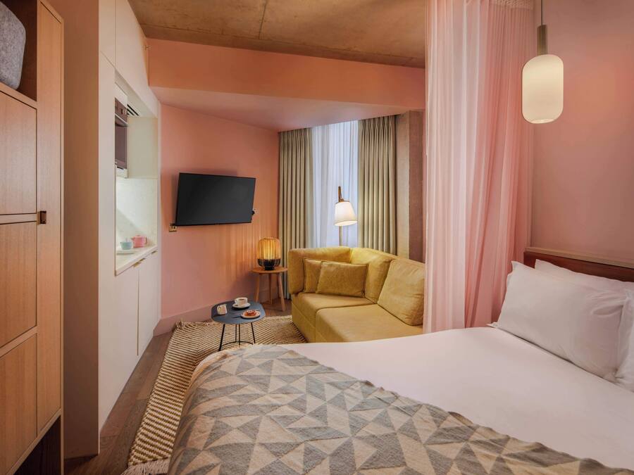 A hotel room with a bed, a sofa, a television, a lamp, and a small table.